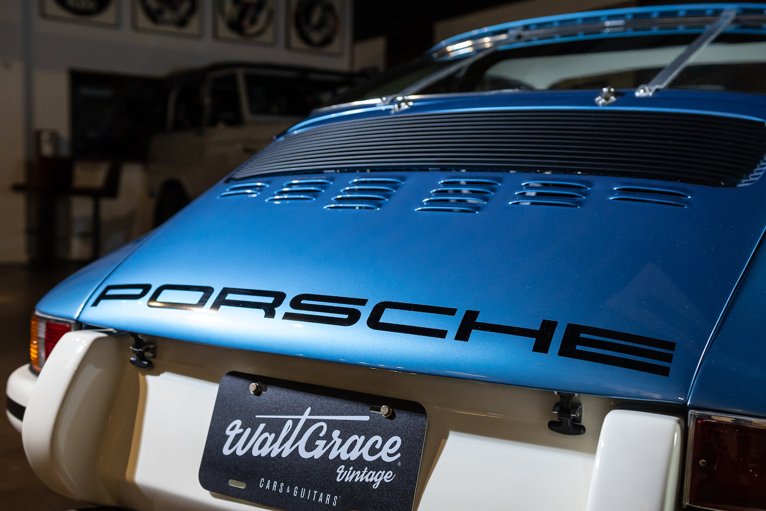 Blue Porsche car with a visible 'Wall Grace Vintage' license plate in a showroom setting.