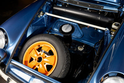 Close-up of a blue car with an open hood revealing the engine and a yellow wheel.