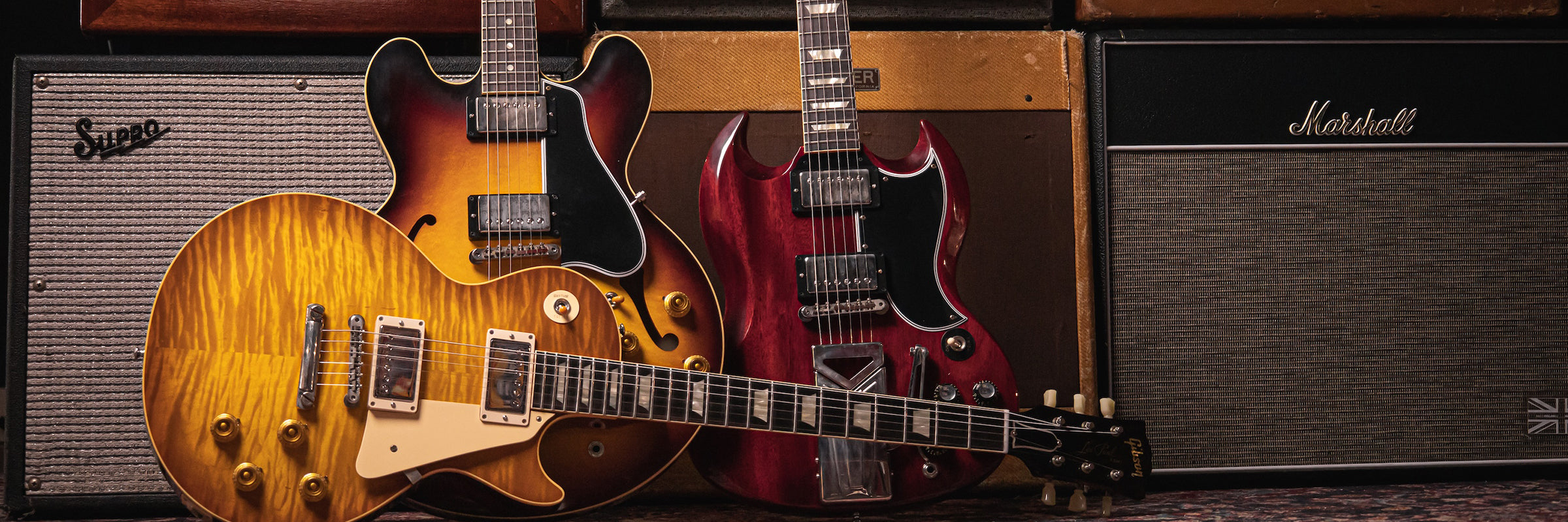 Gibson Electric Guitar Hero Image with ES-335, SG and Les Paul Guitars in front of amps
