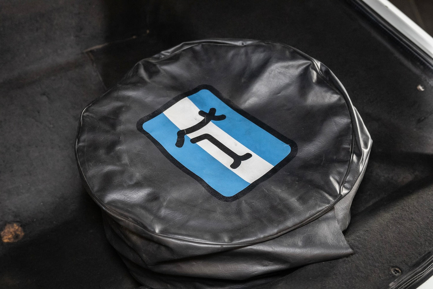 Black tire cover with a blue and white symbol on a black background