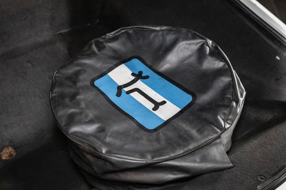 Black tire cover with a blue and white symbol on a black background