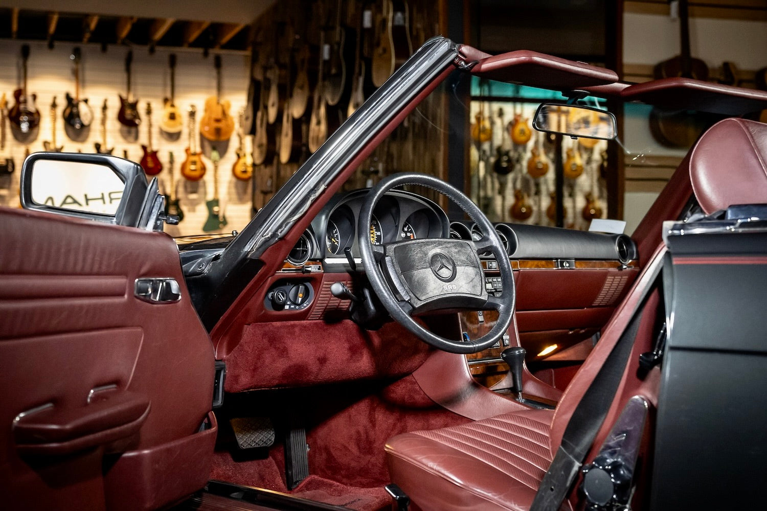 Car interior with a steering wheel and dashboard, set against a guitar store background.