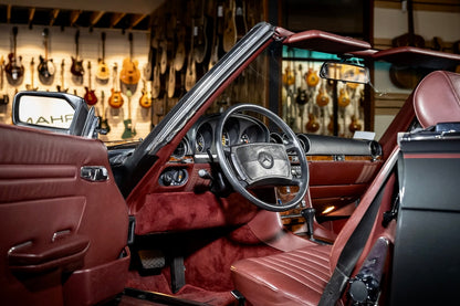 Car interior with a steering wheel and dashboard, set against a guitar store background.