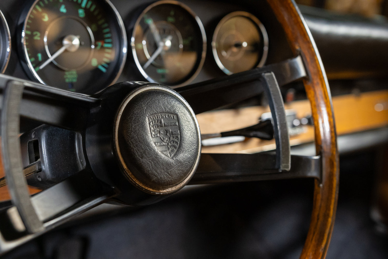 Close-up of a vintage car dashboard with gauges and steering wheel emblem.