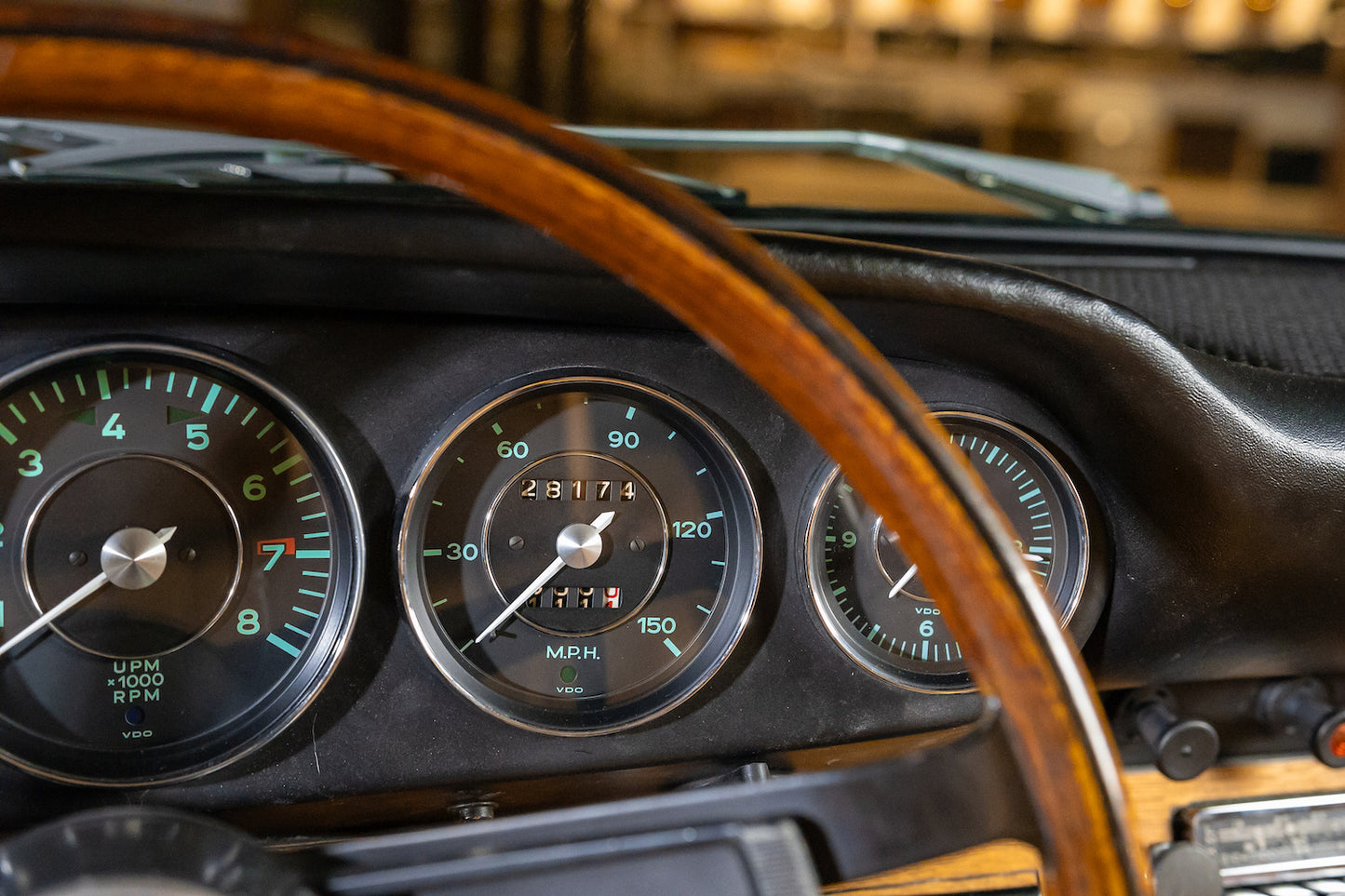 Close-up of a vintage car dashboard with wooden steering wheel and gauges.