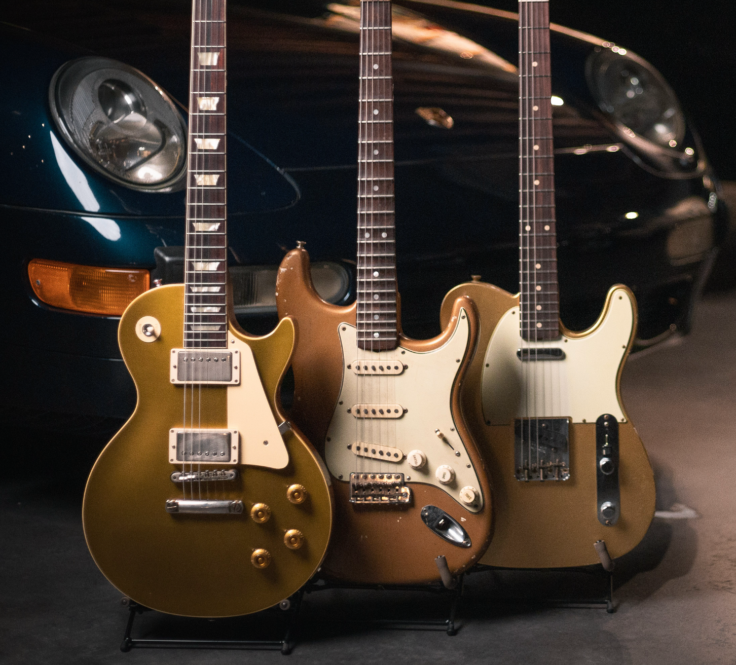 Three electric guitars in front of Porsche