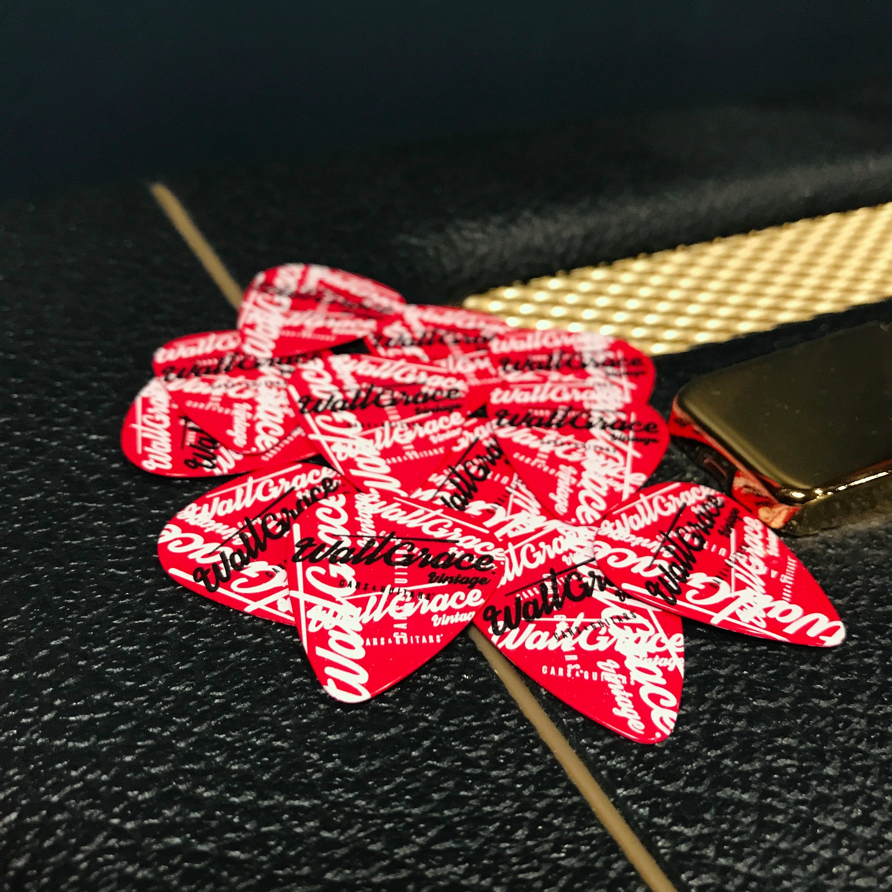 A pack of red and white guitar picks with 'Walt Grace Vintage' branding placed on a guitar amplifier.